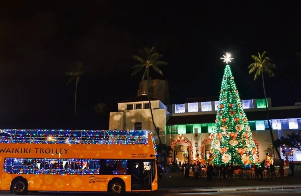 The Waikiki Trolley Holiday Lights Tour bus decorated with Christmas lights in front of a Christmas tree in Honolulu, Hawaii