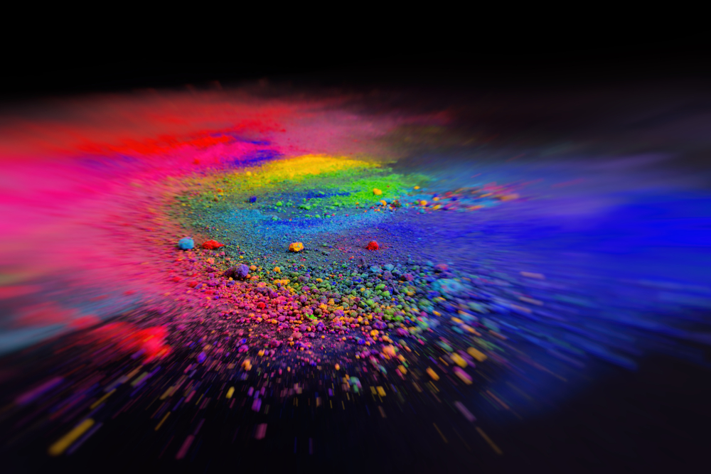 Explosive burst of colorful powder particles radiating from the center, creating a dynamic rainbow-like spectrum of vibrant colors against a dark background, with a motion-blurred effect suggesting rapid movement and dispersion
