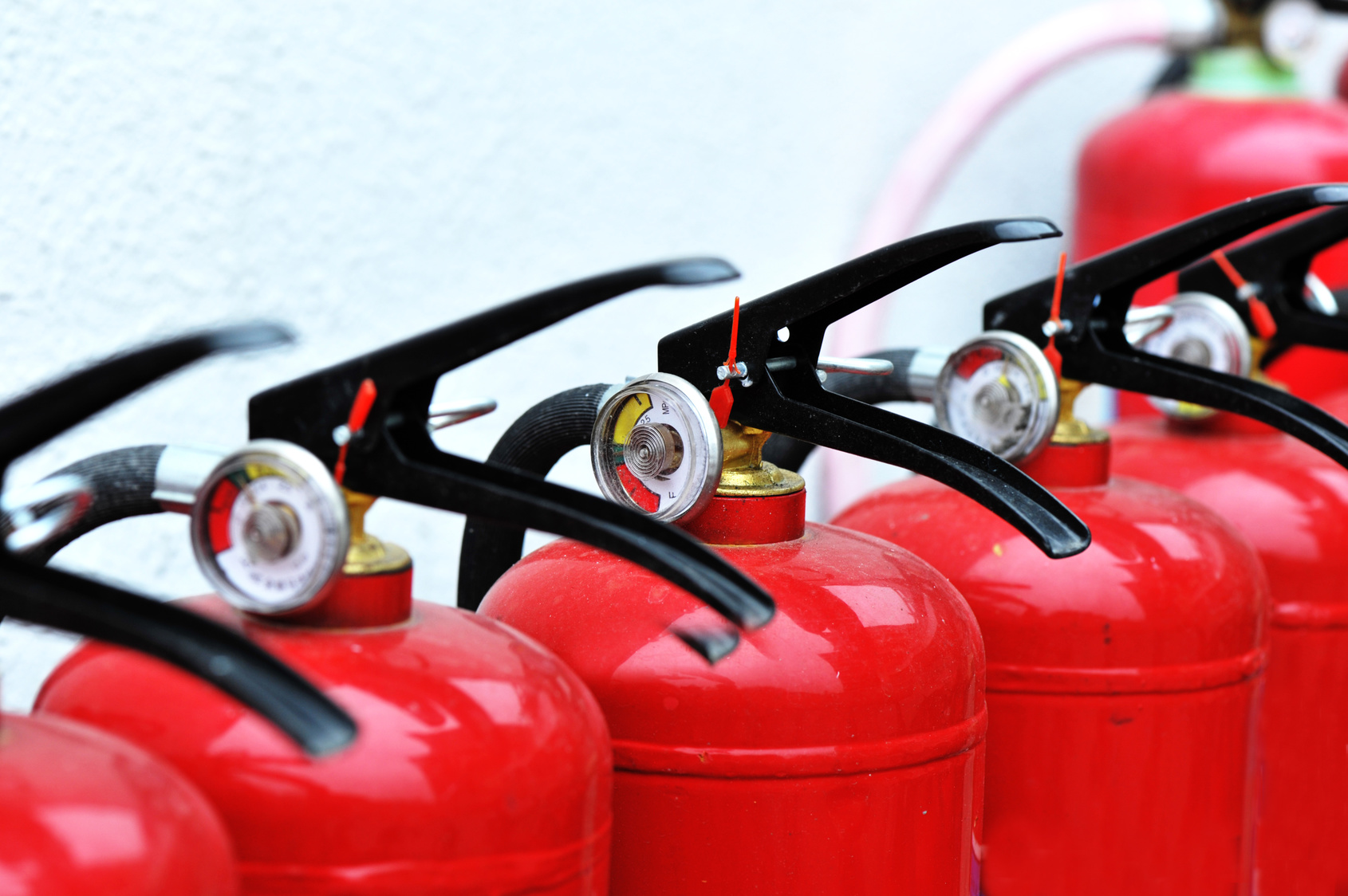 Close-up of red fire extinguishers with black safety handles and pressure gauges, lined up in a row showing detailed safety equipment