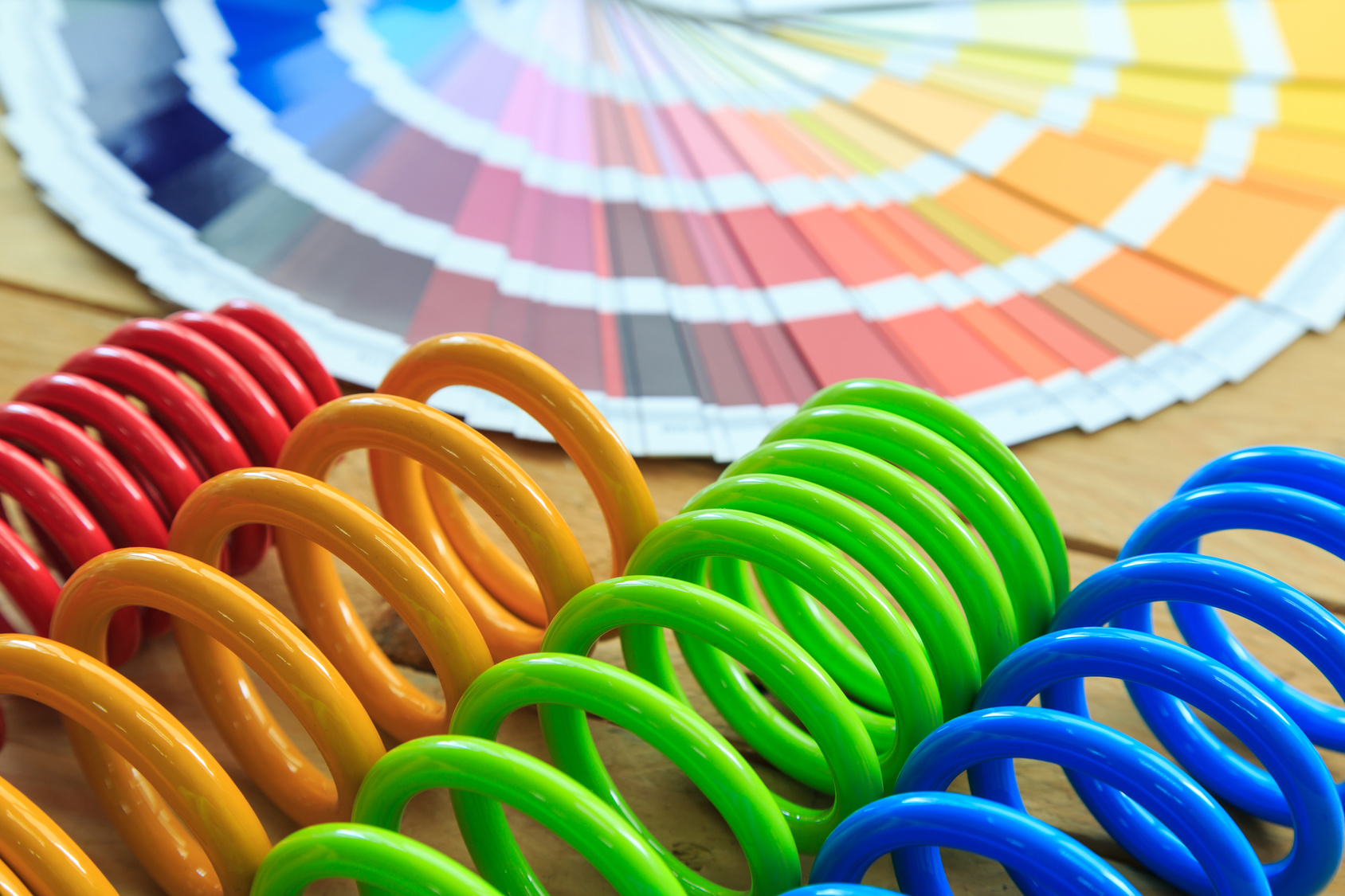 Colorful coiled springs in red, yellow, green, and blue arranged beside a vibrant color swatch fan showcasing a wide range of color options