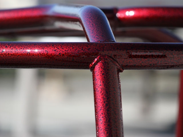Glossy red metal tubes with a speckled powder-coated finish, showcasing precise metalwork and vibrant surface coating technique