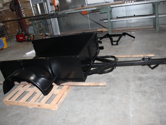 Large black industrial equipment with a sleek powder-coated finish, mounted on a wooden pallet in a warehouse or industrial workshop setting, showcasing precision metalwork and manufacturing capabilities