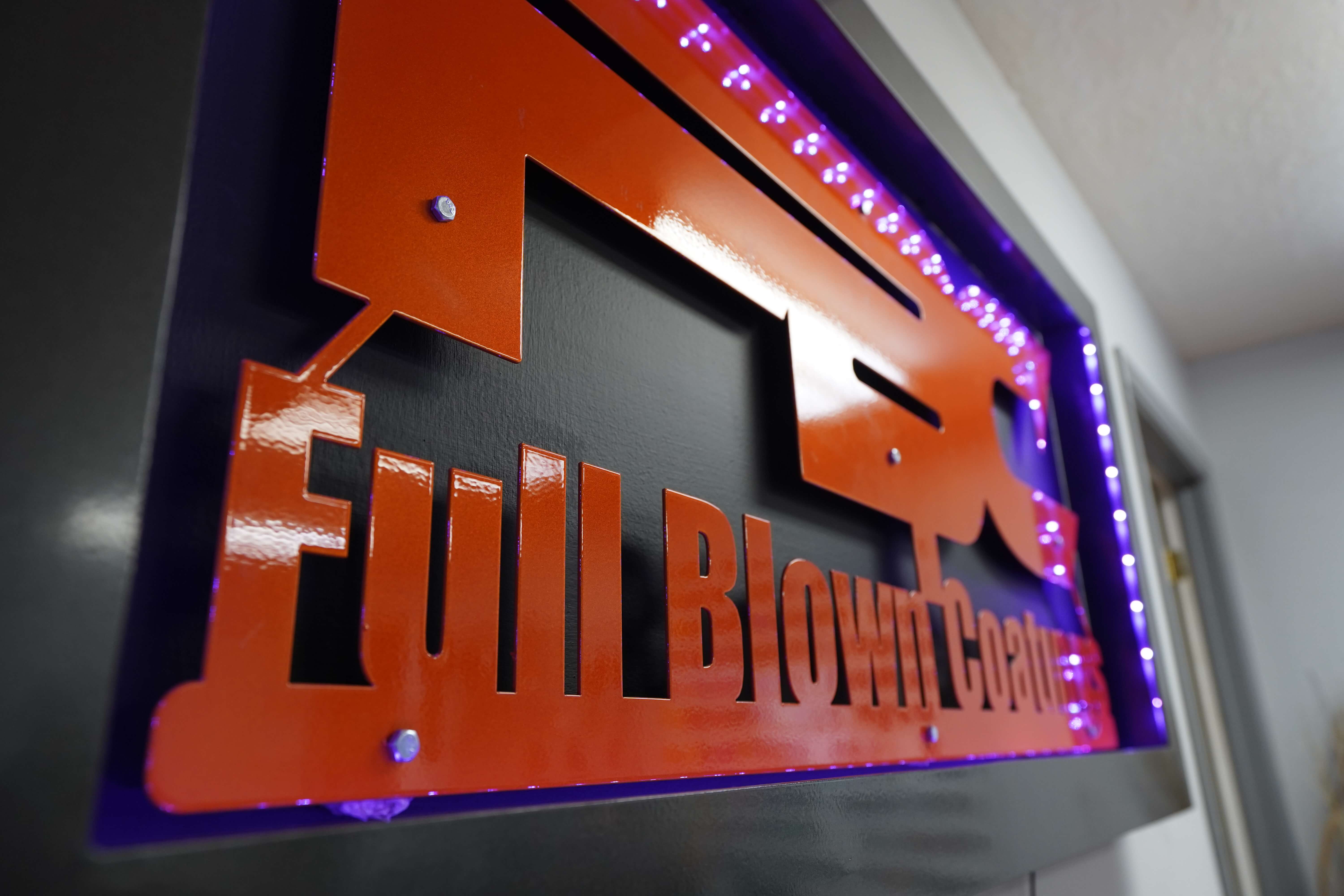 Close-up of a custom metal sign for Full Blown Coatings, mounted on a wall with LED lights.