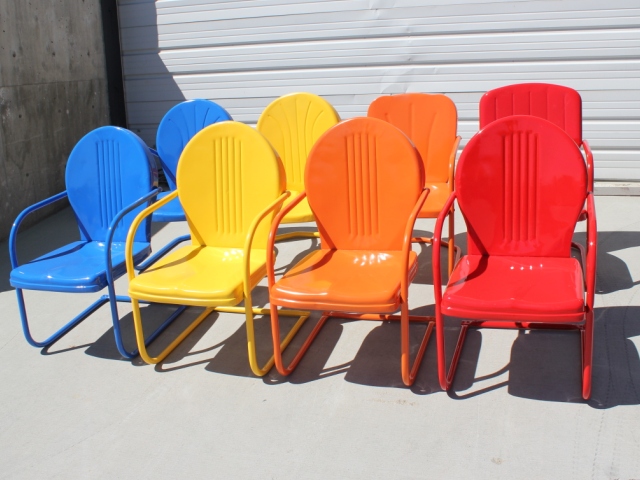 Five vintage-style metal lawn chairs arranged in a row, painted in vibrant colors from blue to red, showcasing a gradient of bright hues against a white garage door background