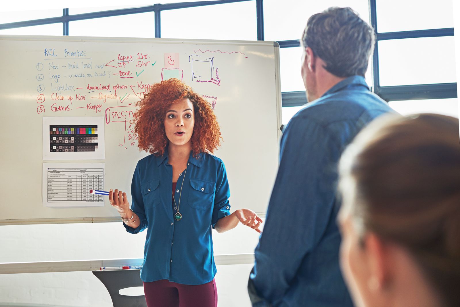 woman standing in front of a whiteboard taking suggestions from colleagues