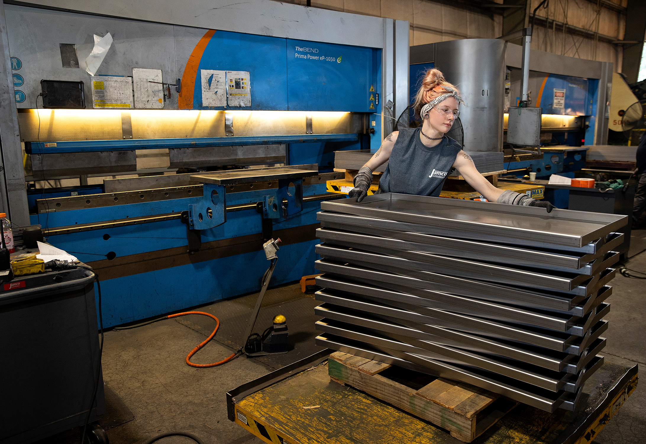 A female employee is working in a fabrication center. She is using tools and is wearing protective equipment. She appears confident in the work she is doing.