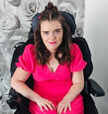 a young women called rachel cracknell who is sat down in her electric wheelchair wearing a beautiful pink dress
