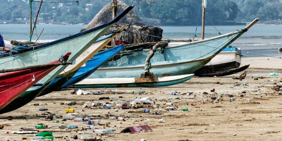 trash on a beach with fishing boats pulled up on the sand