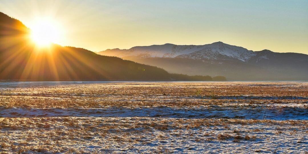 sun rising over a mountain with a flat, frozen, treeless landscape in front
