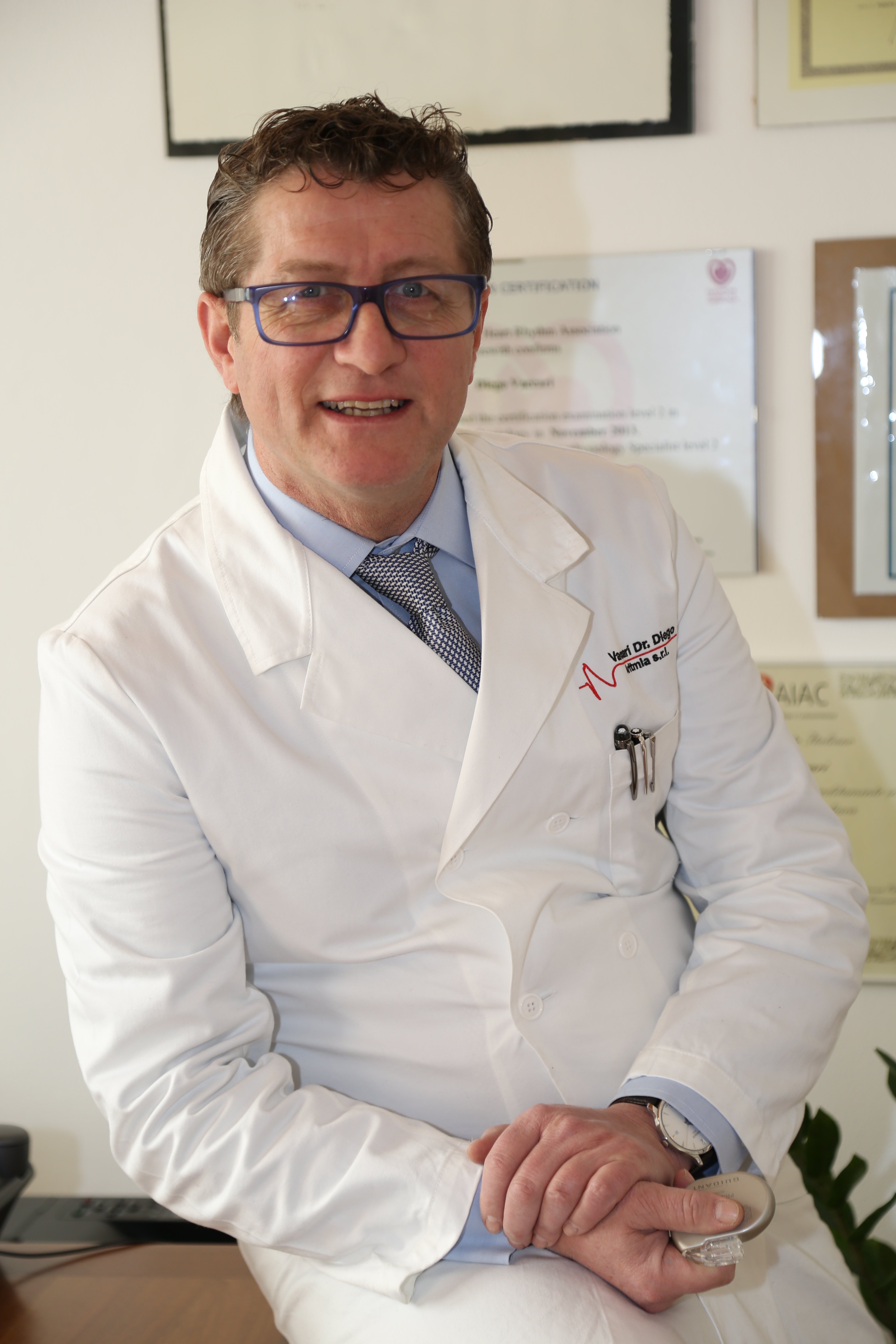 Un uomo che indossa una polo nera sorride e sta in piedi davanti a un muro bianco.