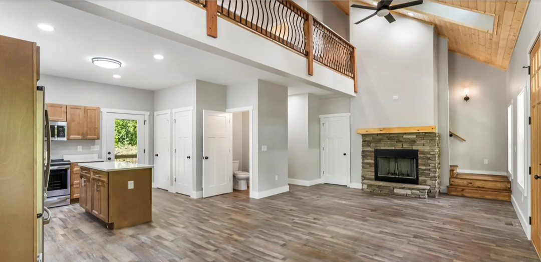 Finished residential interior with open living area, kitchen, loft railing, and fireplace completed by Foothills Construction and Restoration Services in Asheville, NC. Call (828) 484-0160.