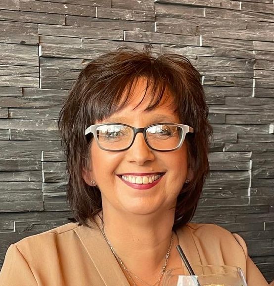 a lady called joanna astley sat down wearing glasses in a restaurant in front of a grey textured tiled wall.