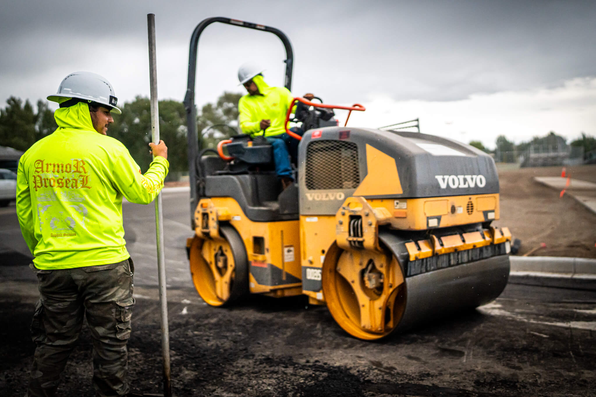 Armor Proseal crew members in safety gear operating a Volvo roller compactor on a fresh asphalt paving project in Montrose, CO, demonstrating professional equipment and safety standards.