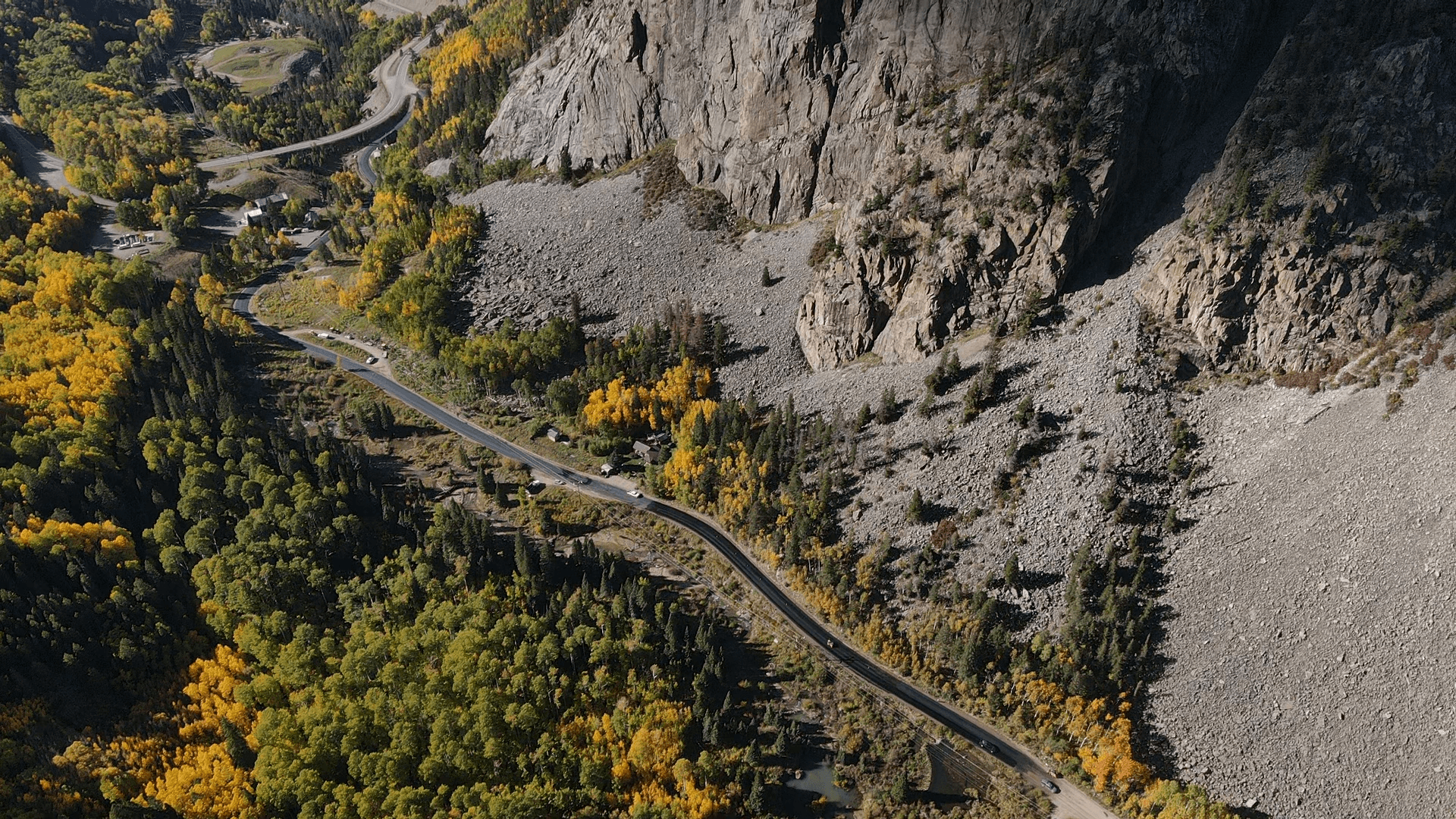 Aerial view of asphalt road winding through Grand Junction's scenic mountain landscape with fall foliage, demonstrating Armor Proseal's paving work in challenging terrain.