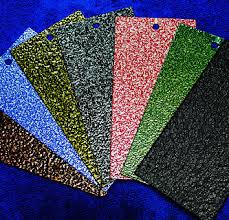 This is a close-up image of powder coating color samples arranged in a fan display. Multiple textured powder coating finishes are shown in various colors including blue, yellow, silver/gray, red/pink, green, and black. The samples appear to be metal plates or chips with different powder coating textures and colors applied, demonstrating the range of finish options available for metal coating projects. The samples are displayed against a deep blue background, highlighting the different color and texture variations possible with powder coating technology.