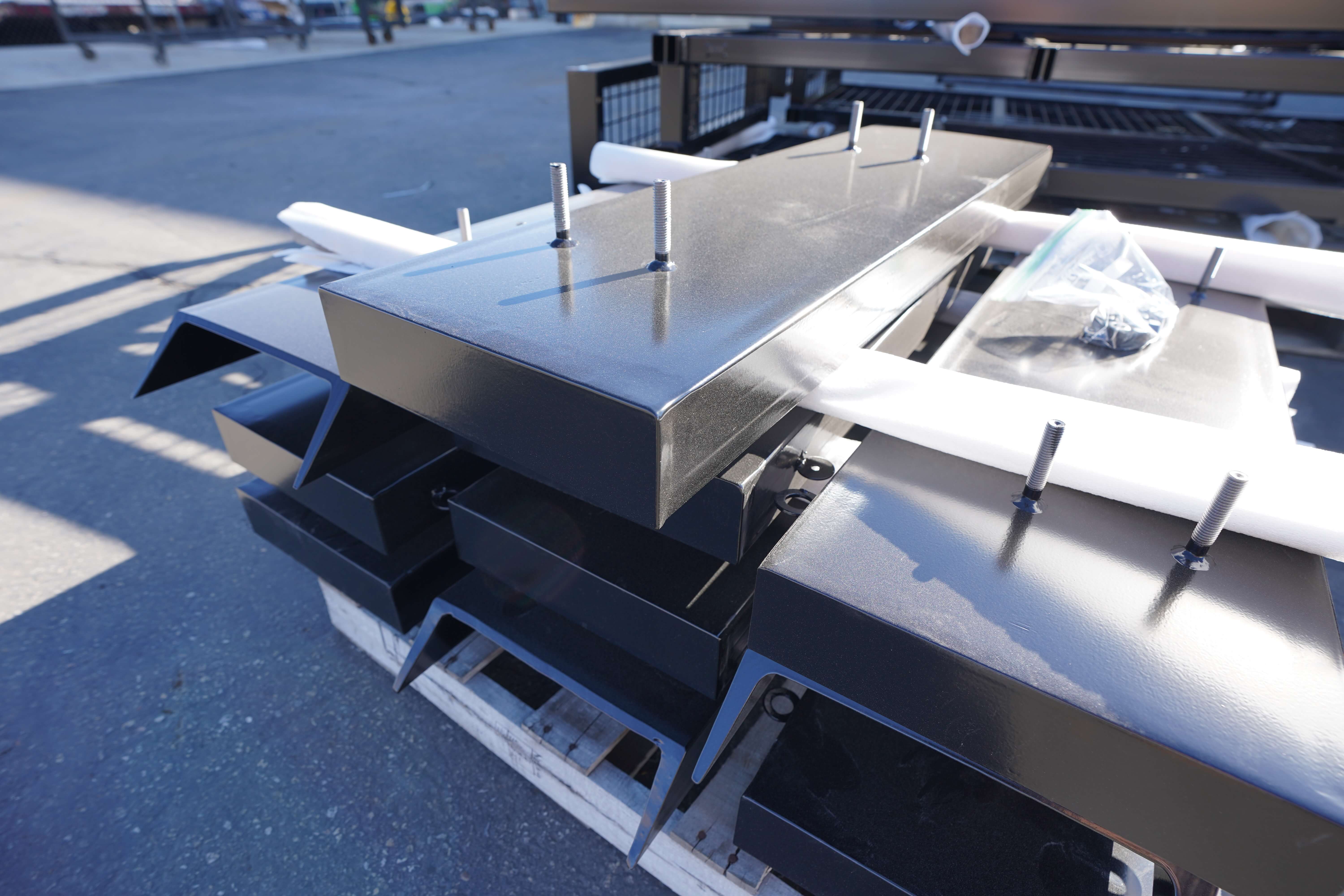 Powder-coated metal parts organized on a pallet, bolts protruding from the surface.