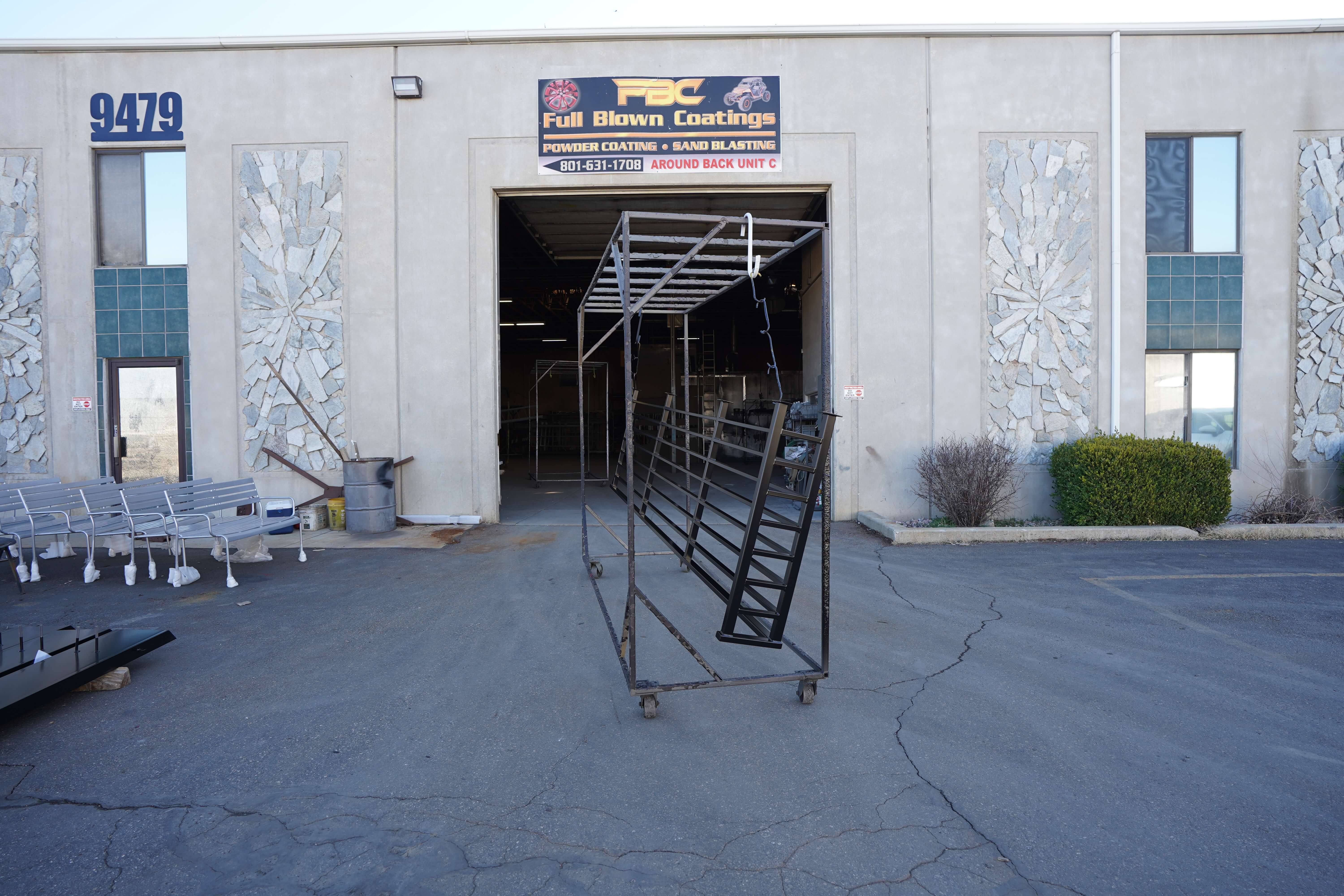 Front view of Full Blown Coatings workshop with metal frames and equipment outside.