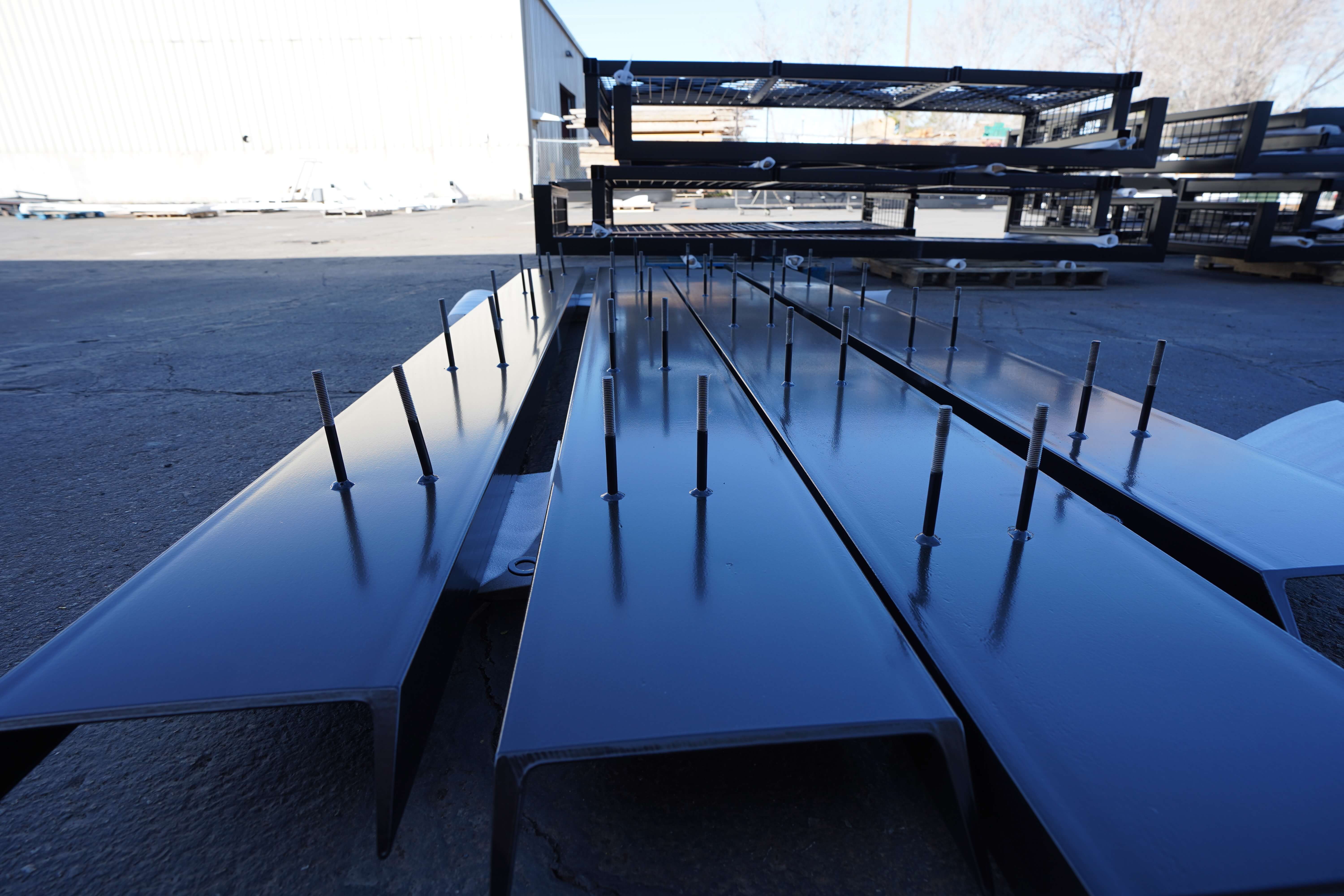 Close-up of glossy black powder-coated metal beams with bolts, laid out on the ground.