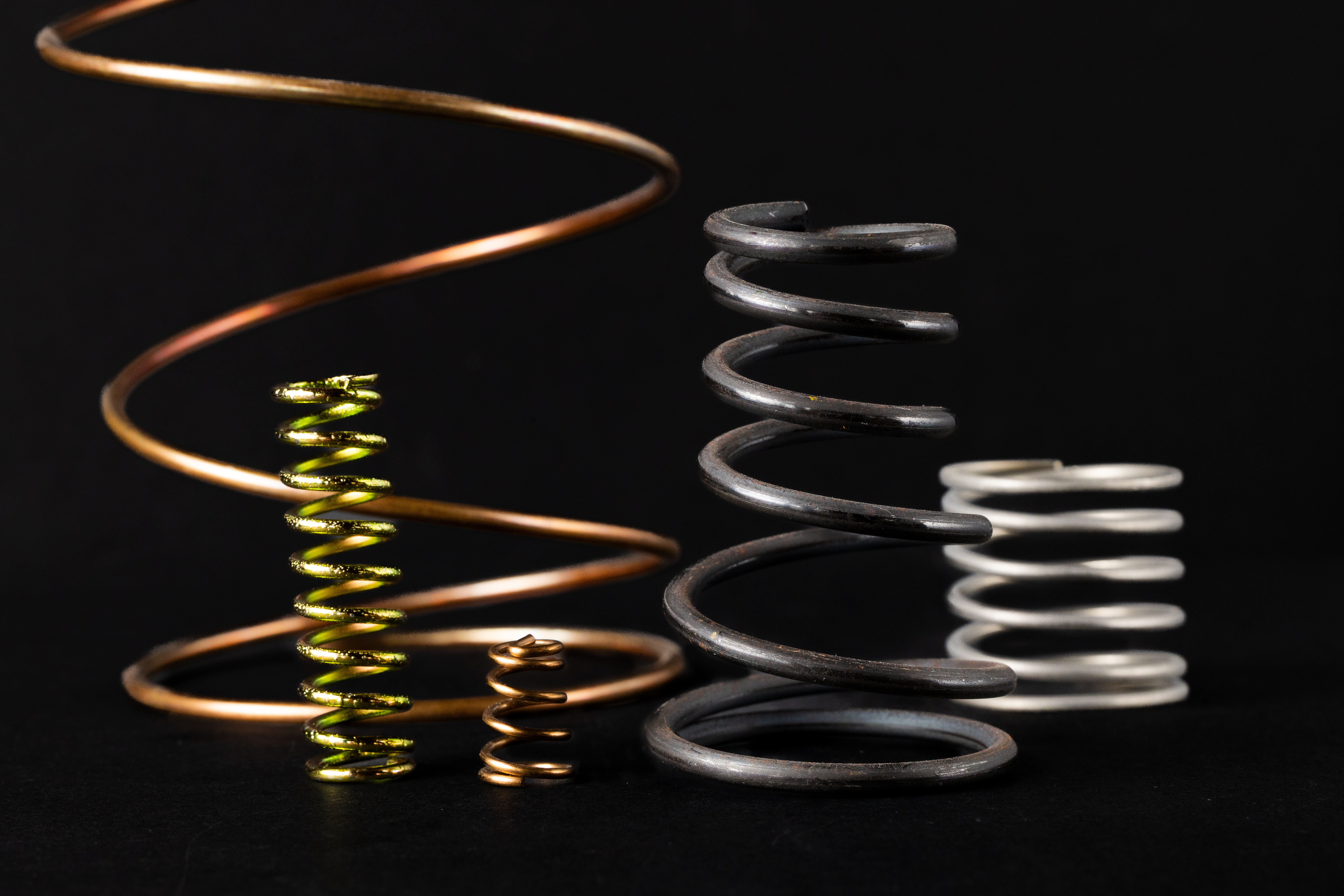 Coiled springs of varying sizes and colors on a black background, including copper, gold, black, and silver.