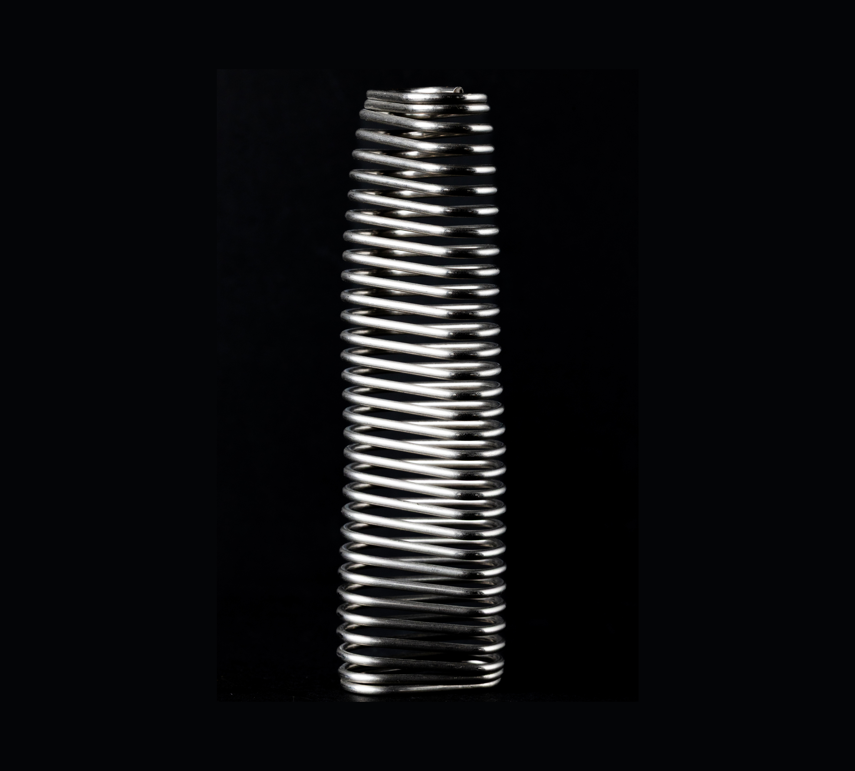 A tightly coiled metal spring against a black background.