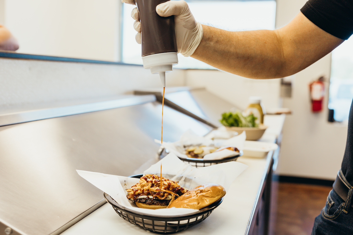 Man Squirting BBQ Sauce on Sandwich at The Old Neighborhood Cafe.