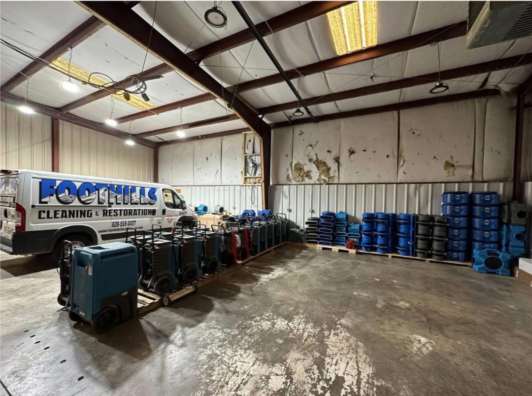 Warehouse interior showing restoration equipment and service vehicles operated by Foothills Construction and Restoration Services in Asheville, NC. Phone (828) 484-0160.