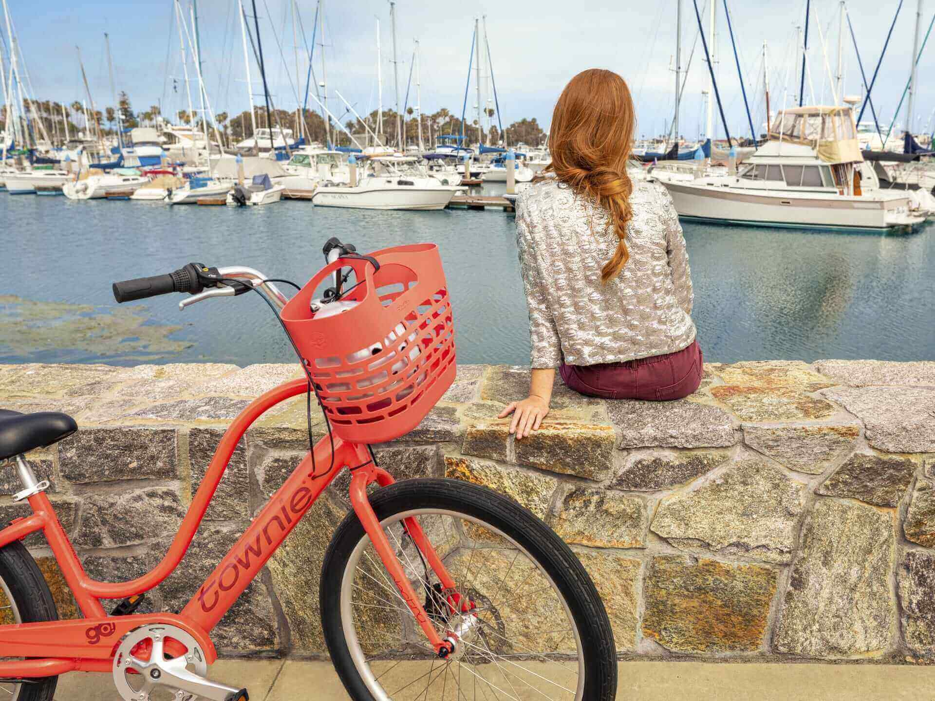 A young woman looking at the scenery of the bay with townie electra ebike parked next to her